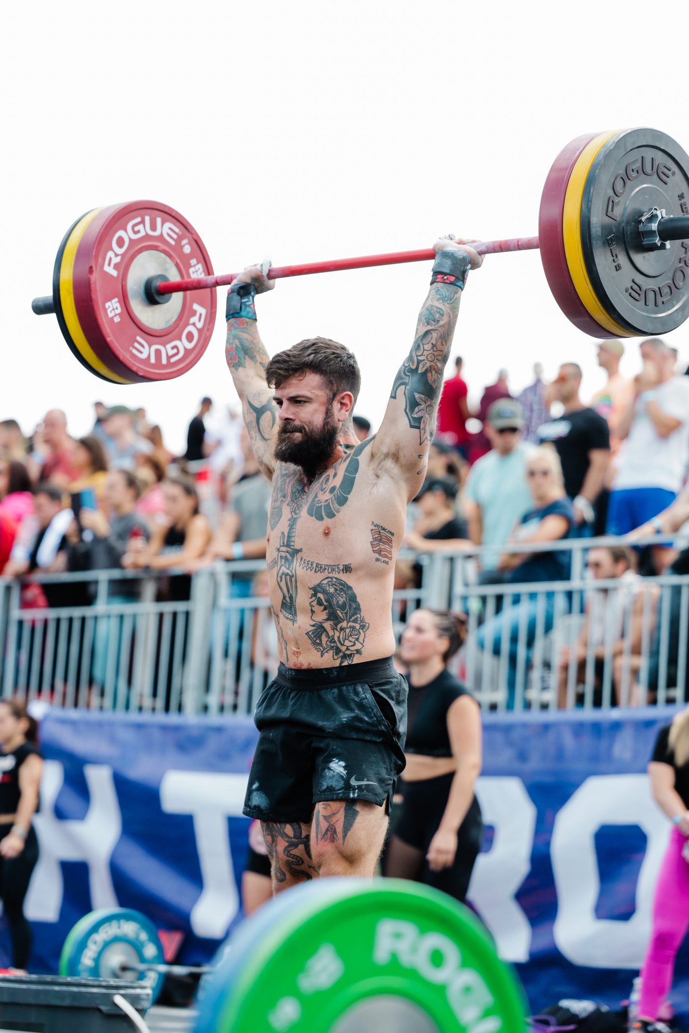 Scott Britton lifting a barbell overhead in front of a crowd at a competition